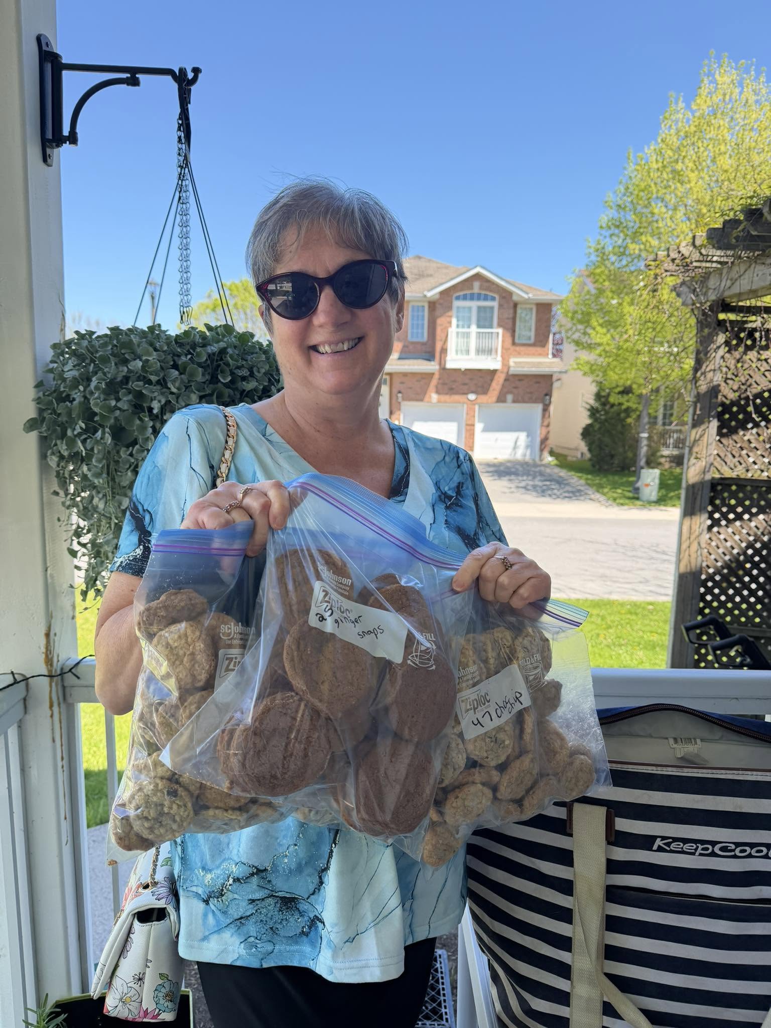 A volunteer on her porch holding up two big bags of home-baked ginger snaps and chocolate chip cookies