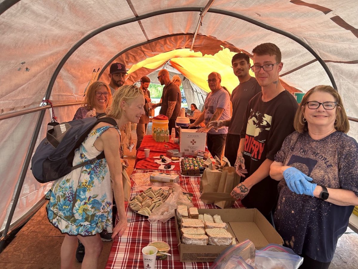 A big group of volunteers gathered around a buffet table loaded with sandwiches, bread and cake inside the Belle Park tent