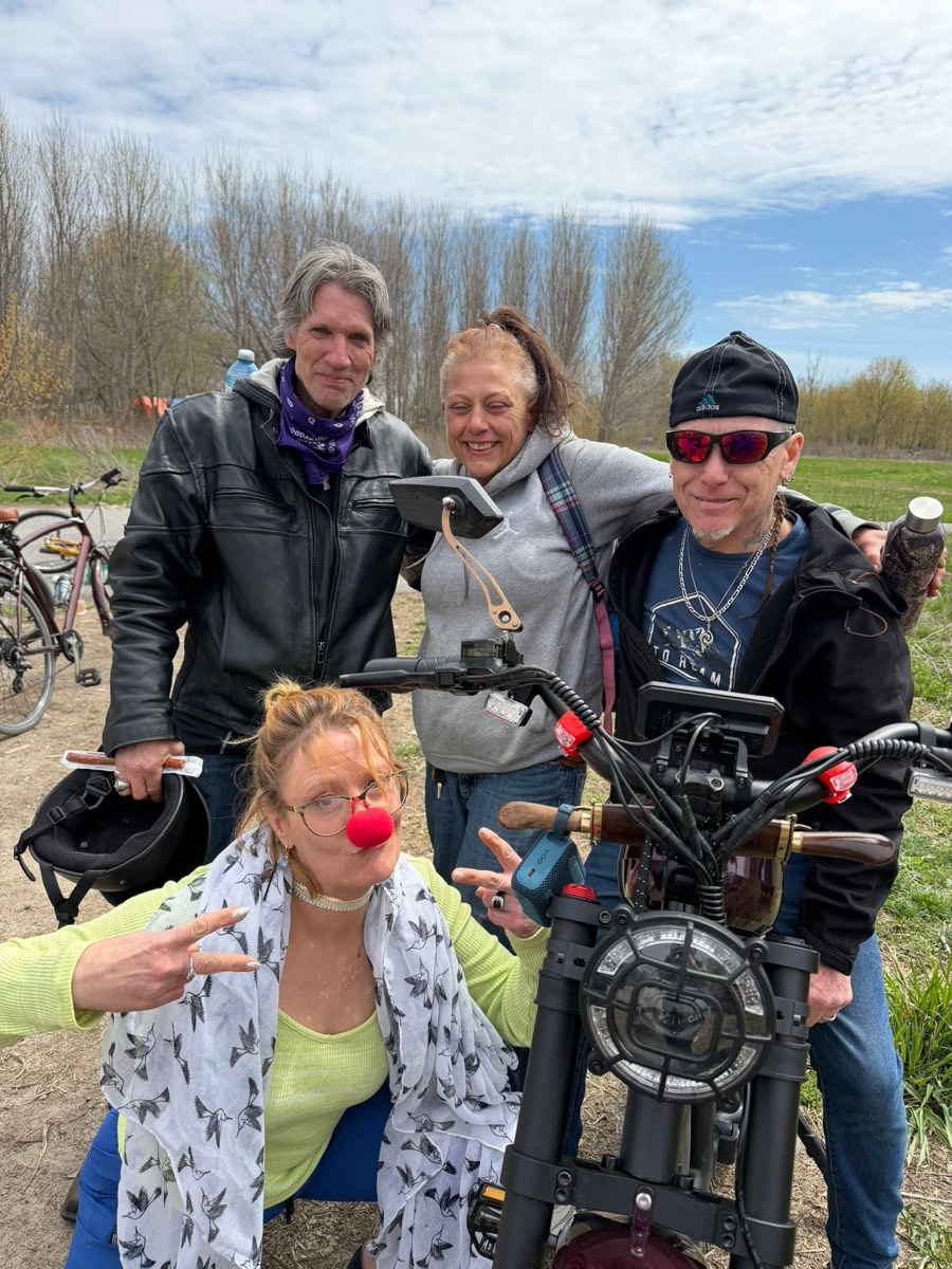 Four community members pose together with a custom motorbike, one wearing a red clown nose