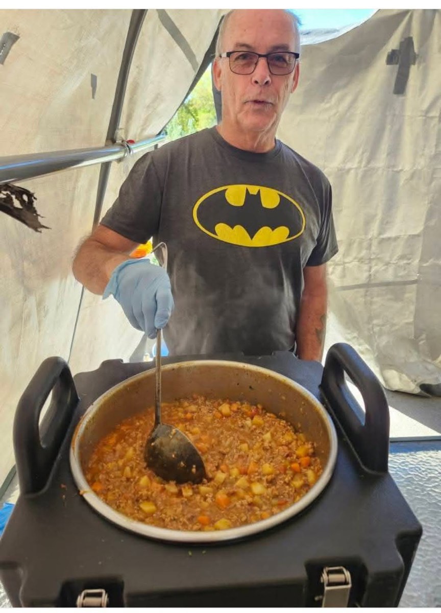 A volunteer in a Batman t-shirt stirs a large pan of chili inside the tent