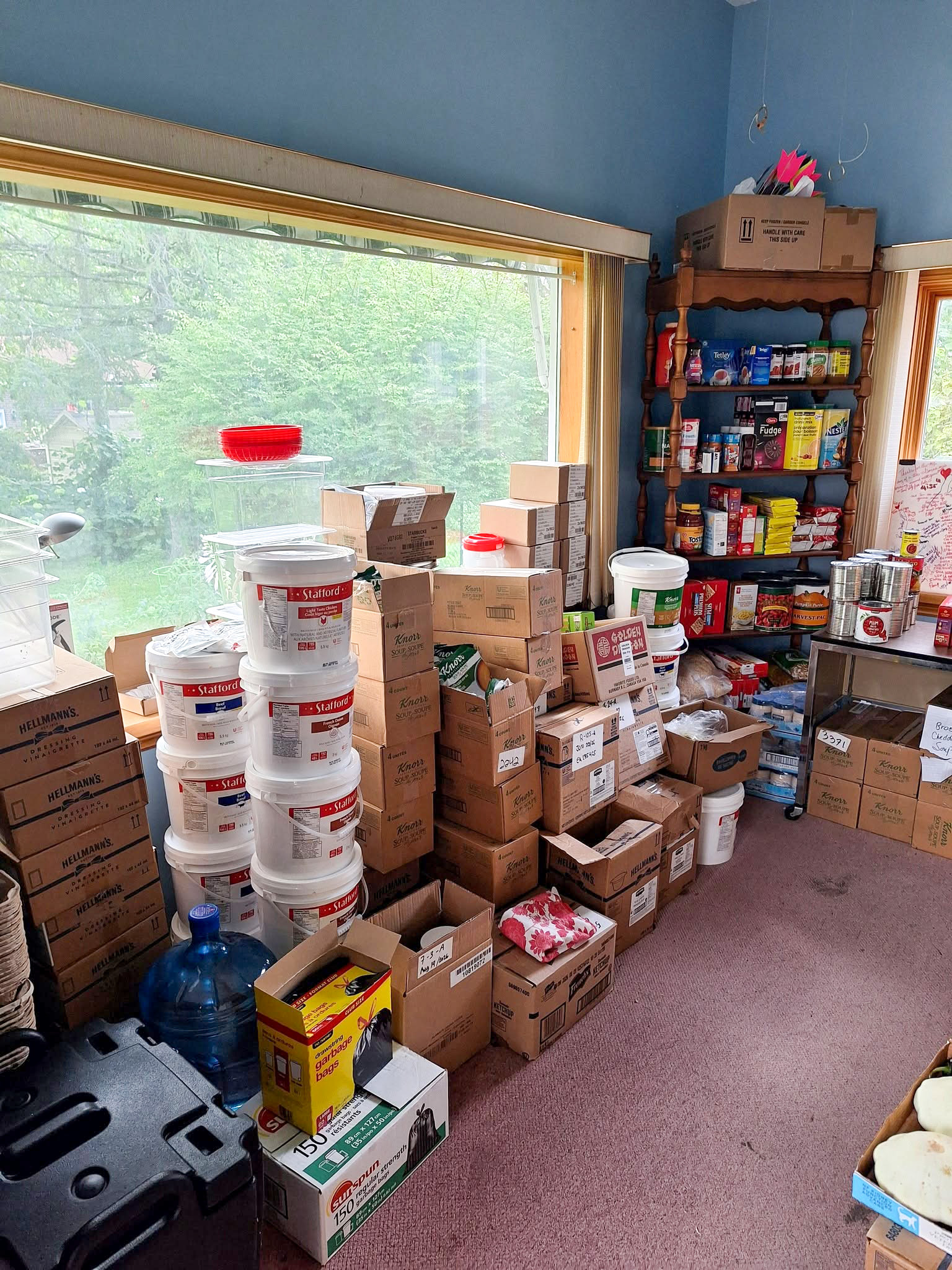 Boxes of dry ingredients, bulk containers and canned food stacked beside shelves of supplies.