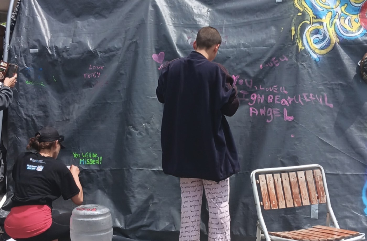 Two community members writing tribute messages in chalk marker on the mural wall at Belle Park