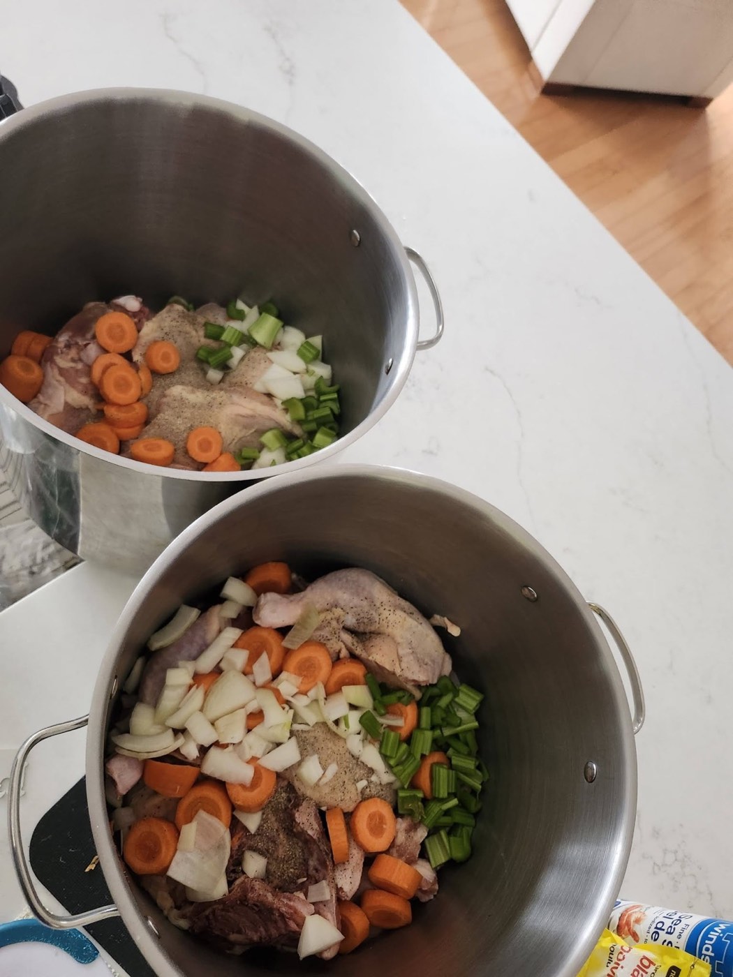 Two large stockpots filled with raw chicken and chopped vegetables, ready to become soup