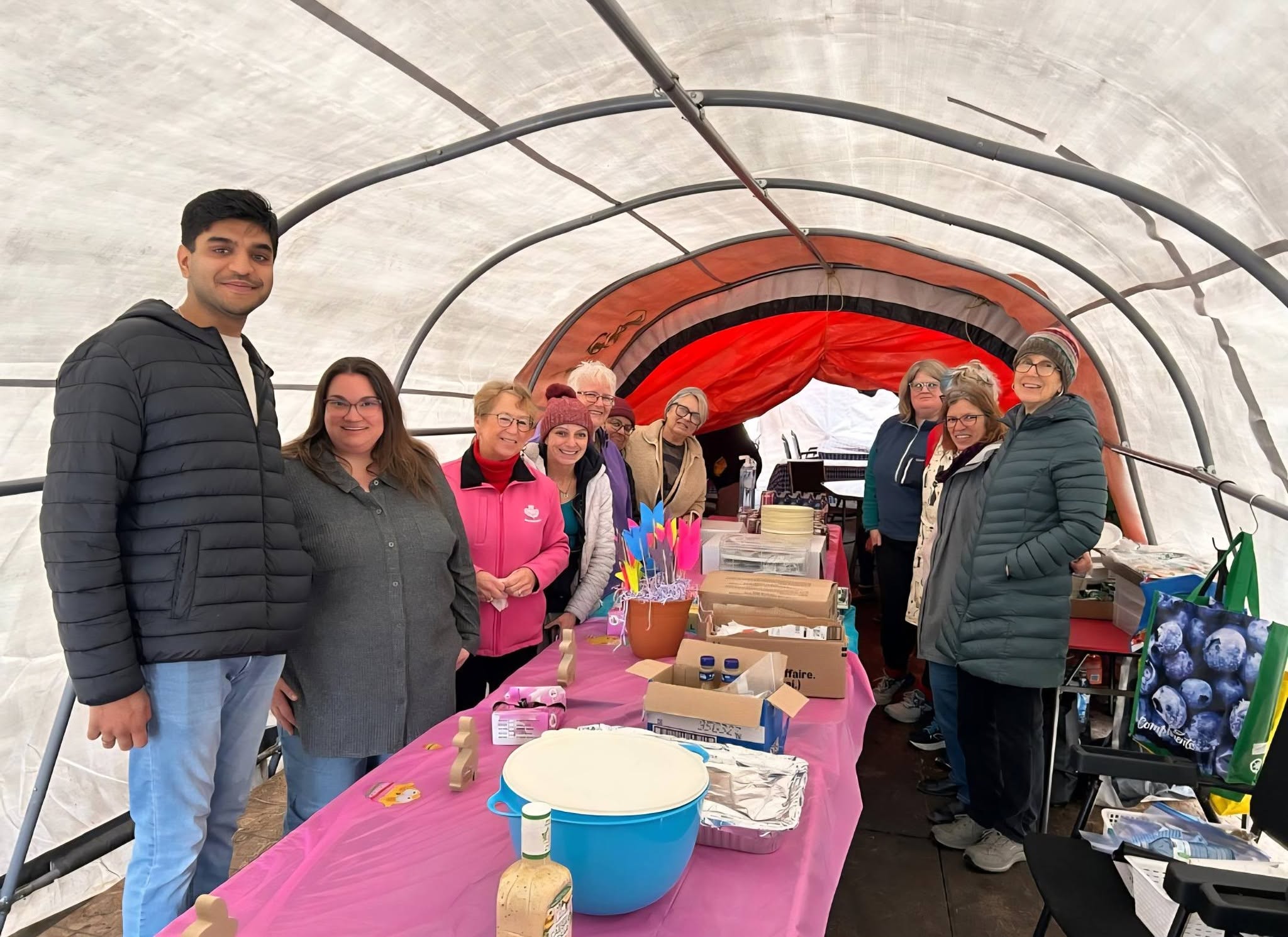 A dozen volunteers standing along both sides of a long table inside the Belle Park tent, ready for a service